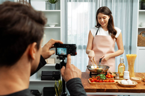 Cameraman opname aan vrouw in chef-kok influencer gastheer koken spaghetti met vlees topped tomatensaus omgeven ingrediënten recept, presentatie van speciale schotel gezond voedsel in de moderne studio. Postulaat. - Foto, afbeelding