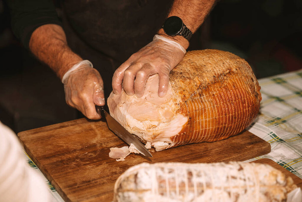 Las manos del chef cortan expertamente un gran jamón asado - Foto, Imagen