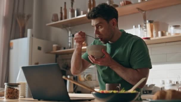 Homem focado tomando café da manhã lendo laptop na cozinha closeup. Unshaven cara sério comer granola olhando para a janela em casa luz moderna. Freelancer calmo almoçando sozinho em casa - Filmagem, Vídeo