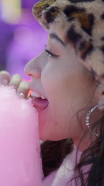Cara de linda hembra joven mordiendo pegajoso color rosa hilo de azúcar en el parque de atracciones - FullHD Vídeo vertical - Imágenes, Vídeo