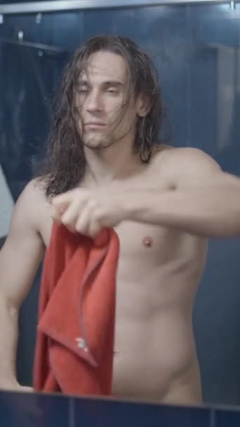 Nuori metroseksuaali mies kuivaus hänen hiukset edessä kylpyhuone peili suihkun jälkeen punainen pyyhe - Lähi laukaus - Pystysuora video - Materiaali, video