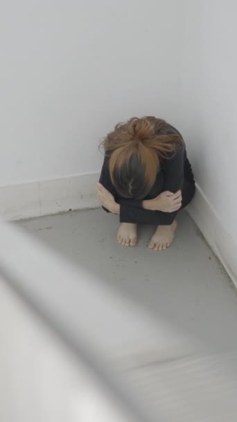 Jonge bange vrouw zit opgerold in hoek van het trappenhuis, van boven - 1080 Verticale video - Video