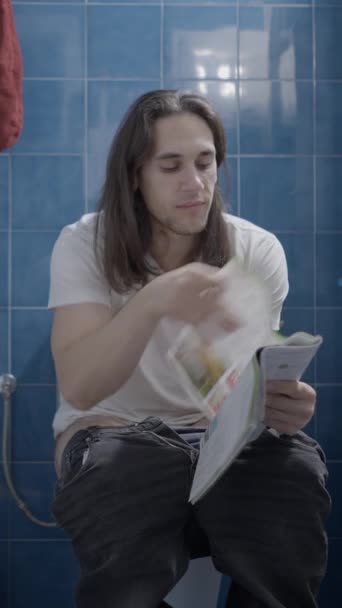 Young caucasian man reading a newspapper and smiling while shit - Frontal shot - Vertical video - Metraje, vídeo
