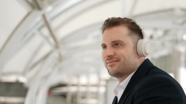 Zbliżenie biznesmena, który przesuwa głowę do muzyki, relaksując się przy słuchawkach. Kaukaski menedżer nosi słuchawki, słuchając i poruszając gestem w miejskim mieście Urbane. - Materiał filmowy, wideo