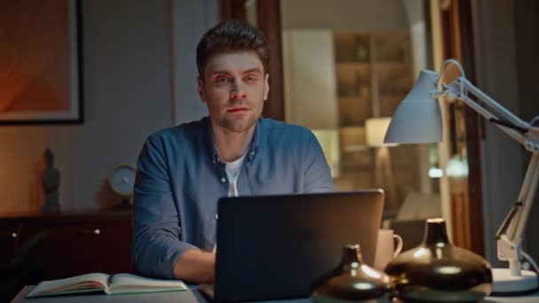Portrait smiling worker posing at night home table closeup. Happy relaxed businessman looking camera working laptop at evening workplace. Brunette calm guy making freelance work at computer desk alone - Footage, Video