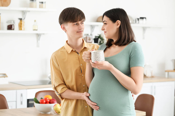 Jeune femme enceinte avec une tasse de thé et son mari dans la cuisine - Photo, image
