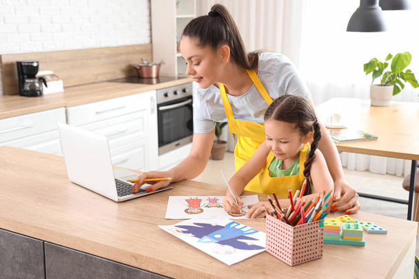 Маленькая девочка со своей работающей матерью рисует на кухне - Фото, изображение