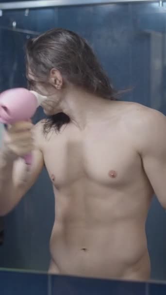 Uomo metrosessuale completamente nudo utilizzando un asciugacapelli davanti allo specchio del bagno dopo una doccia - Inquadratura centrale - Video verticale - Filmati, video