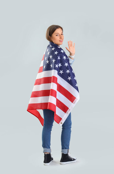 Krásná mladá žena s vlajkou USA mává rukou na světlém pozadí - Fotografie, Obrázek