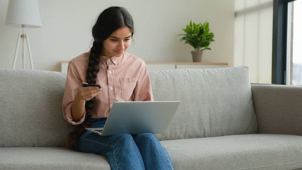 Kadın müşteri çevrimiçi banka kredi kartıyla alışveriş yapıyor dizüstü bilgisayardan mal satın alıyor güvenli finansal internet ödemesi e-ticaret mutlu Arap kız dijital para ödüyor eve internet sitesi siparişi teslimatıyla - Fotoğraf, Görsel