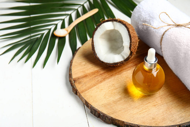 Soporte decorativo con botella de aceite cosmético de coco y toalla de baño sobre fondo de madera blanca - Foto, imagen