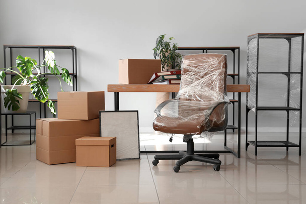 Wnętrze biura z krzesłem owiniętym folią stretch i kartonowymi pudełkami w dniu przeprowadzki - Zdjęcie, obraz