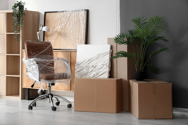Интерьер офиса со стулом, завернутым в стретч-пленку и картонные коробки в день переезда - Фото, изображение