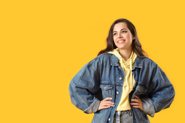 Hübsche junge Frau in stylischer Jeansjacke auf gelbem Hintergrund - Foto, Bild