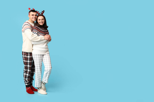 Happy young couple in Christmas pajamas hugging on blue background - Photo, Image