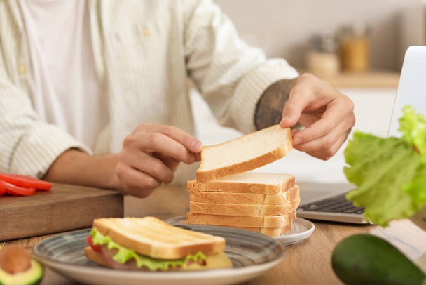 Молодой человек готовит ингредиенты для вкусного сэндвича на кухне, крупным планом - Фото, изображение
