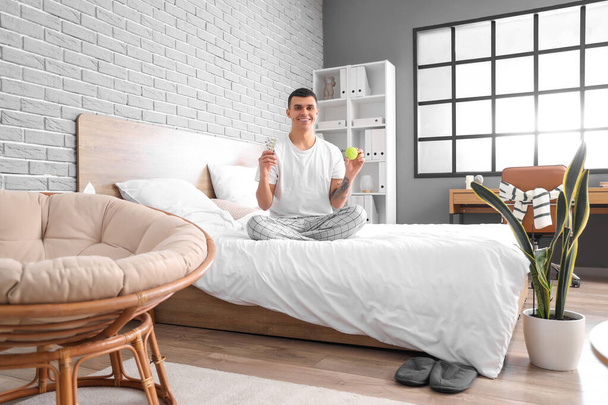 Молодий чоловік з пігулками і таблетками сидить на ліжку в спальні - Фото, зображення
