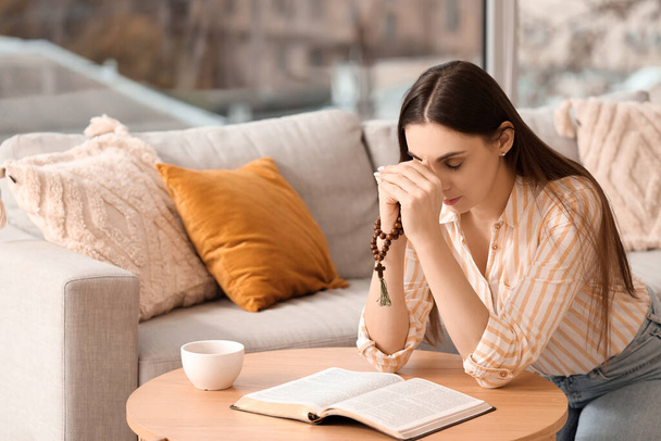 Gyönyörű nő Szent Bibliával imádkozik a kanapén otthon - Fotó, kép