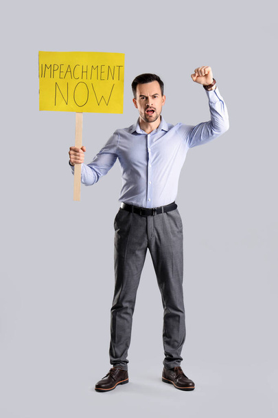 Протест бізнесмен тримає плакат з текстом IMPEACHMENT NOW на світлому фоні - Фото, зображення