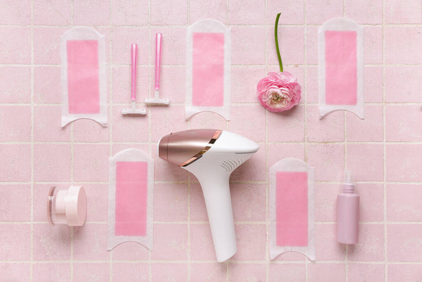 Fotoepiléptica moderna con tiras de cera, maquinillas de afeitar y productos cosméticos sobre fondo de baldosa rosa - Foto, Imagen
