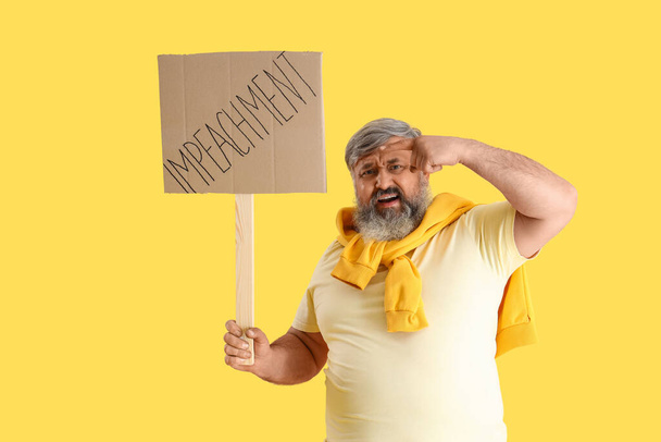 Protesting mature man pointing at placard with word IMPEACHMENT on yellow background - Photo, Image