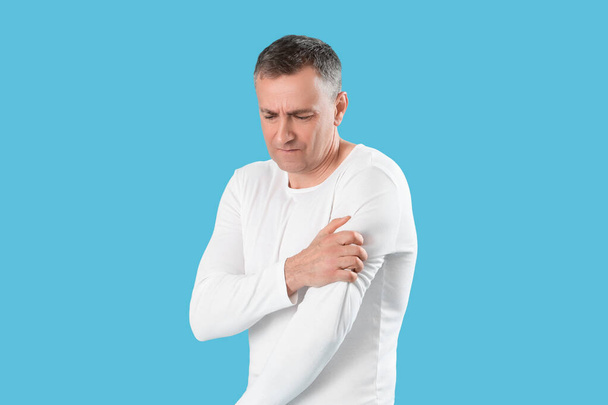 Ώριμος άντρας που υποφέρει από πόνο στον ώμο σε μπλε φόντο - Φωτογραφία, εικόνα