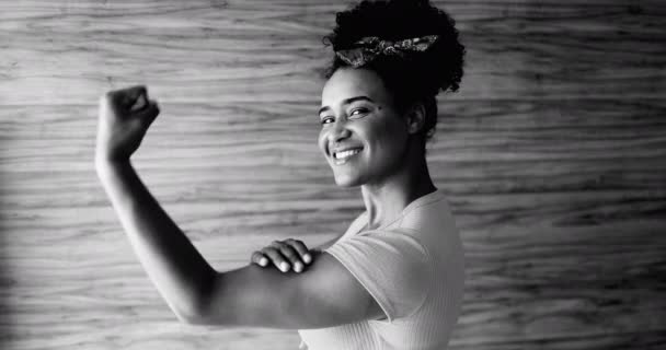 Уверенная в себе молодая афроамериканка демонстрирует силу сгибающей руки и глядя на камеру, одна черная латиноамериканка в черно-белом символизирует "Мы можем это сделать" - Кадры, видео
