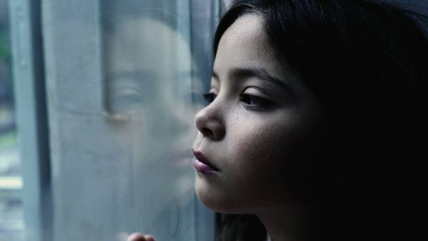 One depressed child leaning on glass window feeling sad and lonely at home, one small introspective girl depicitng childhood mental illness - Photo, Image