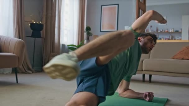 Fit Sportler Workout in der Wohnung. Junger kräftiger Mann, der auf der Sportmatte energisch die Arme seiner Beine in Seitenlage hebt. Muskulös motivierter Kerl Athlet trainiert Körperkraft Ausdauer zu Hause. - Filmmaterial, Video