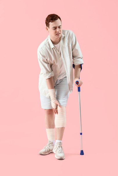 Injured young man after accident with crutch on pink background - Photo, Image