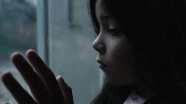Choroba psychiczna z dzieciństwa przedstawiająca małą dziewczynkę zmagającą się z depresją i wartościowością opierającą się na szklanym oknie gapiącą się na widok w humorzastej scenie - Zdjęcie, obraz