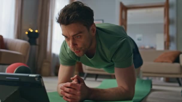 Sportoló keres video tutorial táblagéppel apartman nappaliban. Jóképű motivált férfi néz online edzés leckét sport szőnyeg haza. Egészséges sportoló követi internetes edző edzés. - Felvétel, videó
