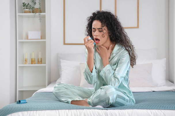 Jonge Afro-Amerikaanse vrouw met astma inhalator in slaapkamer - Foto, afbeelding