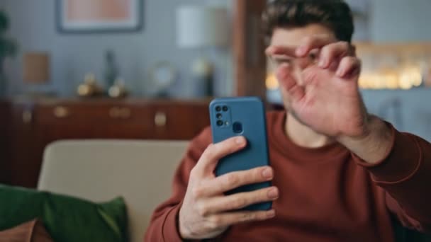 Бізнесмен вітає на відео виклик за допомогою смартфона, який сидить вдома крупним планом. Впевнений чоловік, що зачиняється на екрані мобільного телефону, відповідаючи на відеодзвінок на дивані. Успішний фрілансер махає рукою до веб-камери мобільного телефону - Кадри, відео