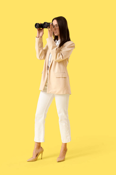 Jeune femme d'affaires regardant à travers des jumelles sur fond jaune - Photo, image