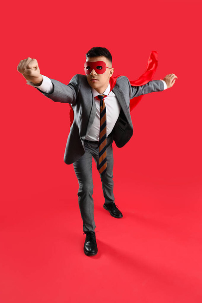 Empresario vestido de superhéroe volando sobre fondo rojo - Foto, imagen