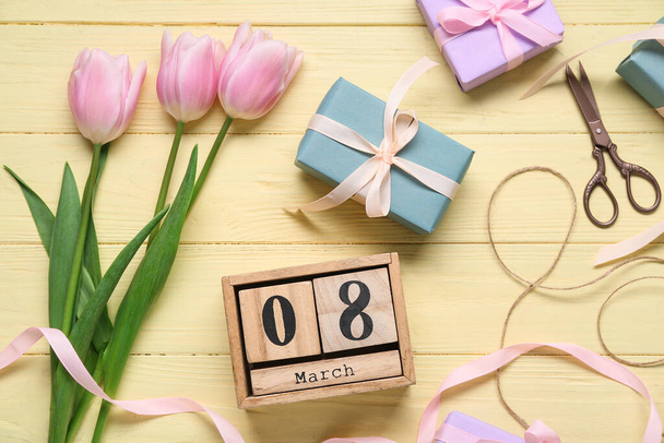 Kalendář kostek s datem 8. března, dárkové krabice, růžové tulipány a nůžky na žlutém dřevěném pozadí. Mezinárodní oslava Dne žen. Horní pohled - Fotografie, Obrázek