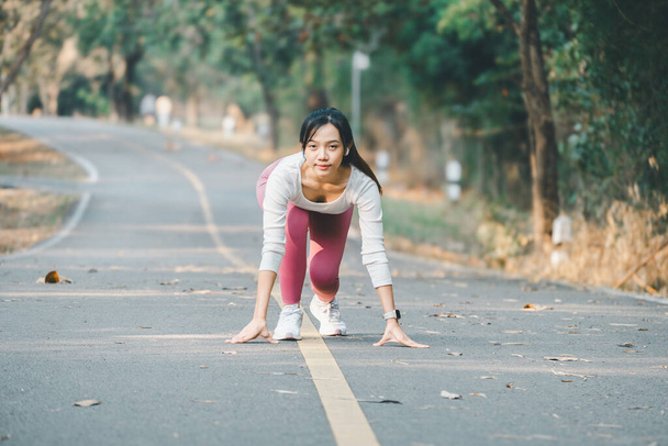 Sport fitness concept, Een gefocuste jonge vrouw in sportkleding maakt zich klaar om te beginnen met haar run op een rustige boomrijke weg. - Foto, afbeelding