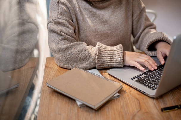 Eine abgeschnittene Aufnahme einer Frau in einem kuscheligen Strickpullover, die aus der Ferne in einem Café arbeitet und an ihrem Laptop arbeitet. Geschäftsfrau, Freiberuflerin, Schriftstellerin - Foto, Bild