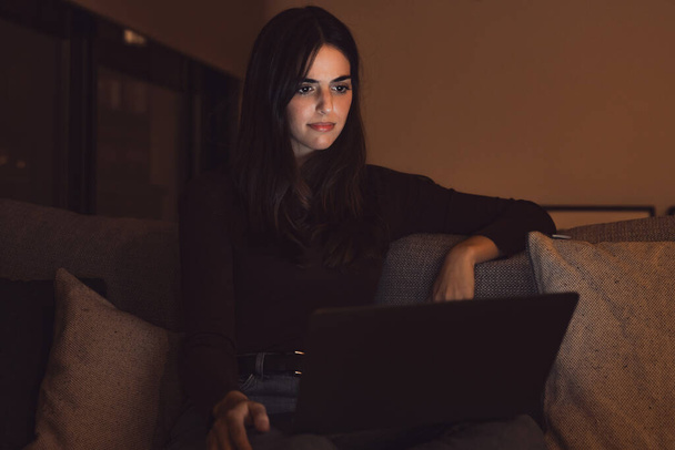 Nieszczęśliwa młoda pracownica spogląda na ekran laptopa zszokowana awarią gadżetu lub problemami operacyjnymi późną nocą. Sfrustrowana kobieta zaskoczona nieoczekiwanym błędem w urządzeniu komputerowym. - Zdjęcie, obraz