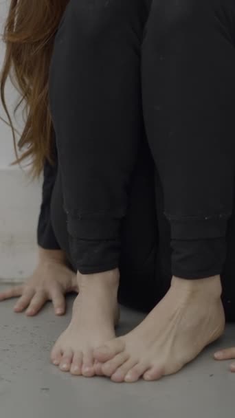 Onherkenbare vrouw zit in de hoek met handen en blote voeten op de vloer - 1080 Verticale video - Video