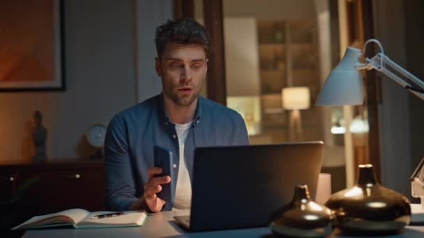 Vakava mies puhuu webcam chat tietokoneella istuu pöydän yöllä lähikuva. Komea liikemies keskustelee työstä kannettavan videopuhelun avulla kotona. Itsevarma kaveri ottaa myöhään liiketoiminnan online-konferenssi - Materiaali, video