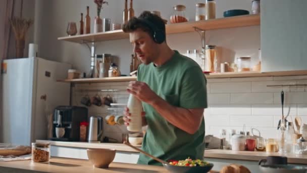 Sluchátka hipster připravuje snídani tanec v útulné kuchyni detailní. Atraktivní mladý muž zpívající oblíbenou píseň ze sluchátek vaření doma. Radostně šťastný melomaniak poslech hudby v dopoledních hodinách - Záběry, video