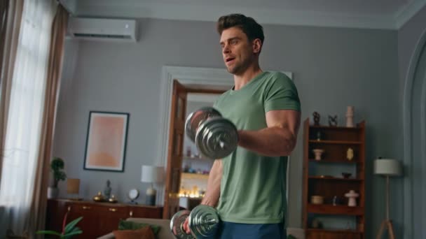 Tensed athlete exercising dumbbells in apartment close up. Focused handsome man lifting sport equipment training powerful hands muscles biceps at home. Healthy sportsman workout for muscular fit body. - Footage, Video
