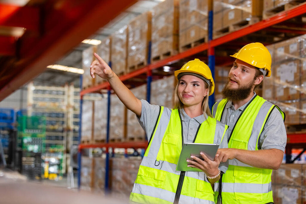 Male and Female professional worker wearing safety uniform using tablet inspect goods on shelves in warehouse. supervisor worker checklist stock inspecting product in storage for logistic. - Photo, Image
