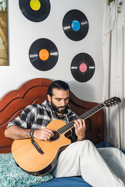 Latinský muž hraje na akustickou kytaru ve svém pokoji. Hudebník s harmonickým nástrojem. - Fotografie, Obrázek