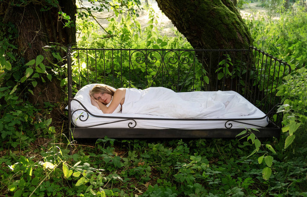Atraktivní, spokojená, mladá, sexy blondýnka ležící v železné posteli na slunci v přírodě pod starými plačícími vrbami - Fotografie, Obrázek