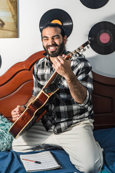 Homem colombiano tocando e estudando guitarra em seu quarto. Instrumento acústico e harmônico. Músico cantando ao usar instrumento harmônico. - Foto, Imagem
