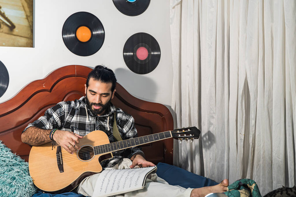 Kolumbijský muž hraje a studuje kytaru ve svém pokoji. Akustický a harmonický nástroj. Hudba. - Fotografie, Obrázek