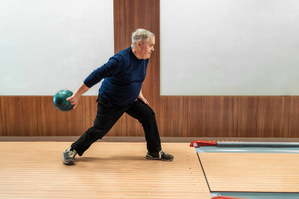 Yaşlı adam bovling topunu yuvarlamaya hazır sakin bir oyunda, aktif bir son sınıf yaşam tarzında. - Fotoğraf, Görsel